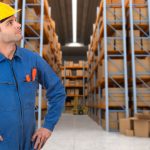 Man with helmet and blue overalls in a warehouse with pallet racking system